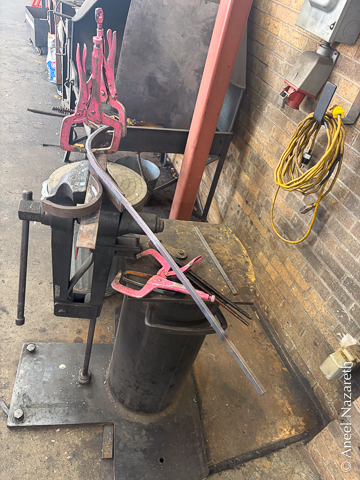 Two vise-grip C-clamps hold one end of the bar to the top part of the jig